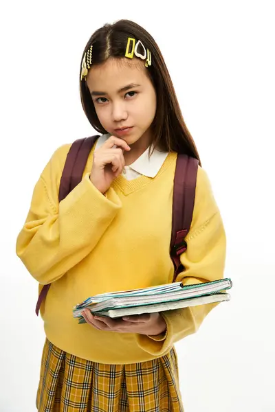 Una studentessa asiatica elegante posa con i suoi libri e lo zaino su uno sfondo bianco. — Foto stock