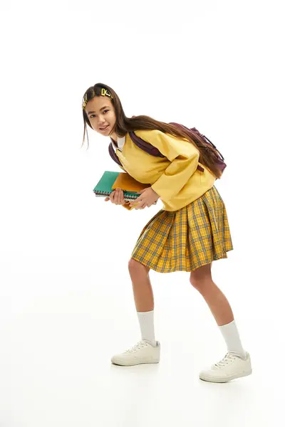 A young asian schoolgirl showcases her trendy outfit while playfully posing in a studio. — Stock Photo