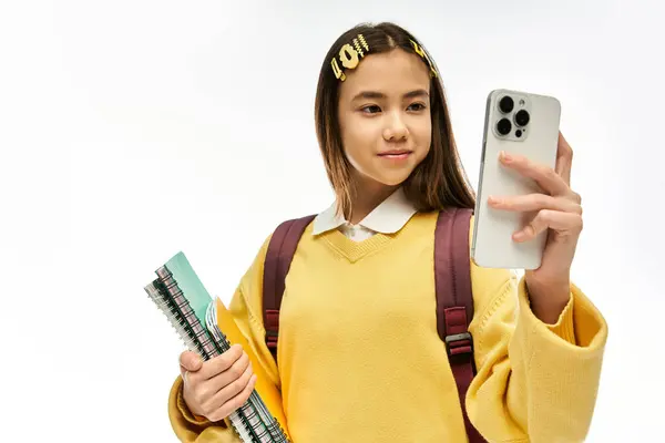 Ein stilvolles asiatisches Schulmädchen posiert in einem Studio, hält Notizbücher in der Hand und macht ein Selfie. — Stockfoto
