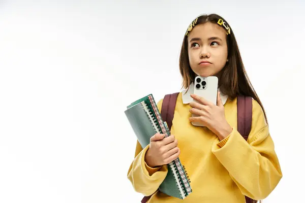 Asiatique écolière vitrine son look élégant tout en tenant des livres et un téléphone dans la lumière du studio. — Stock Photo