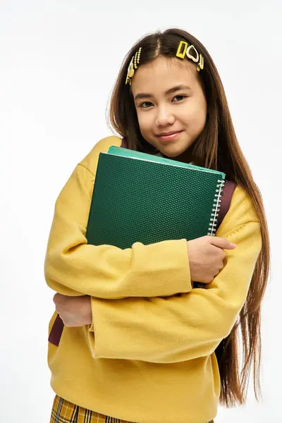 A young Asian schoolgirl embraces her notebook while showcasing her trendy style. — Stock Photo
