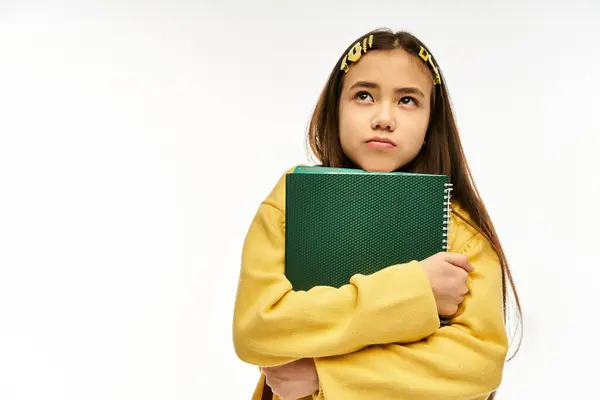 Ein stilvolles asiatisches Teenie-Mädchen in einem Studio hält ein Notizbuch und sieht nachdenklich aus. — Stockfoto