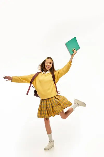 A happy teenager in a trendy outfit strikes a lively pose while holding a book. — Stock Photo