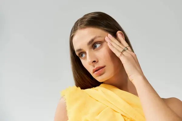 Una giovane donna mette in mostra la sua bellezza, toccandosi delicatamente il viso con un abito giallo vibrante. — Foto stock