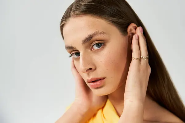 A young woman exudes confidence, touching her hair while posing against a minimalist background. — Stock Photo