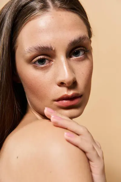 Une jeune femme met en valeur sa beauté naturelle avec un sourire serein, touchant son épaule. — Photo de stock