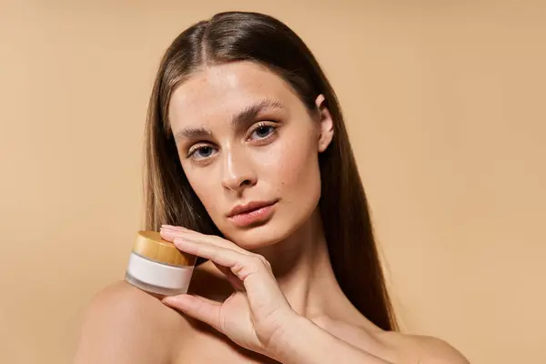 A young woman showcases her flawless skin while holding a skincare product in a serene setting. — Stock Photo