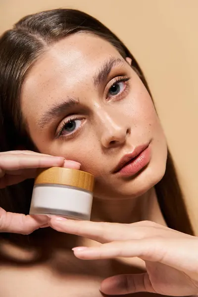 A young woman showcases her radiant skin with a skincare product, exuding summer freshness. — Stock Photo
