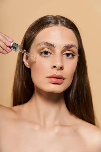 A young woman applies serum to her cheek, embodying elegance and summer glow in a serene setting. — Stock Photo