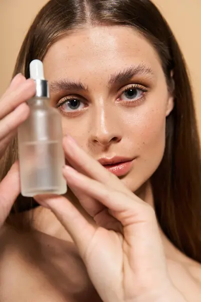 Young woman showcases her radiant skin while holding a skincare serum against a warm background. — Stock Photo