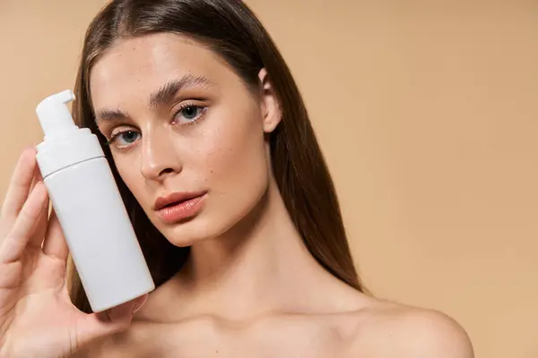Eine schöne Frau posiert anmutig, während sie ein Hautpflegeprodukt vor einem warmen Hintergrund präsentiert. — Stockfoto