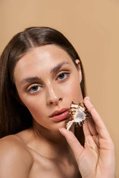 Una joven con la piel radiante muestra una concha de mar, encarnando la belleza natural del verano. - foto de stock
