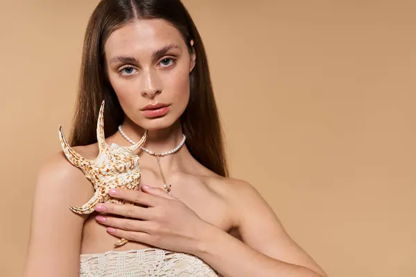 Una joven muestra su estilo veraniego, sosteniendo una concha con elegancia y gracia. - foto de stock