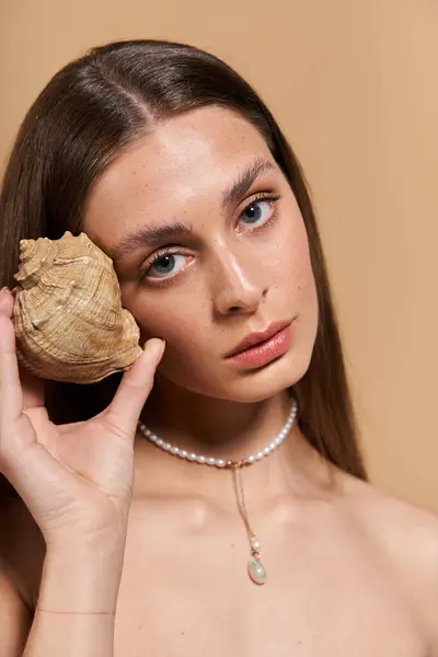 Una joven sostiene una concha al oído, capturando la esencia del verano y la belleza natural. - foto de stock