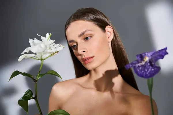 Una joven sostiene hermosas flores blancas y moradas, profundamente pensadas en un cálido día de verano.. - foto de stock
