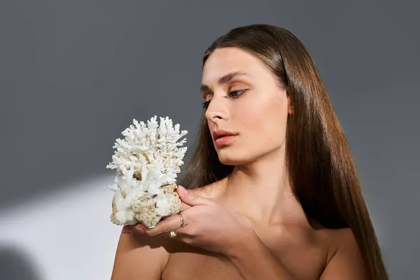 Eine junge Frau hält anmutig ein einzigartiges Korallenstück in der Hand, das ihre sommerliche Eleganz unterstreicht. — Stockfoto