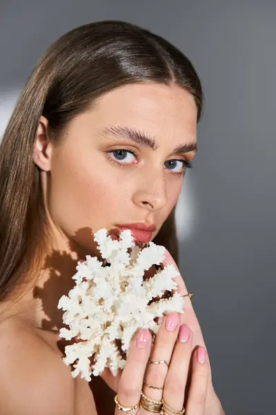 Una joven mujer sostiene una delicada pieza de coral, exudando belleza y vibraciones de verano en un entorno elegante. - foto de stock