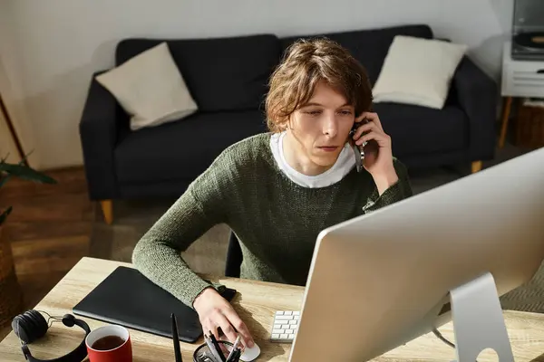 Un joven estudiante está en casa, multitarea entre una llamada telefónica y estudiar en un ordenador. - foto de stock
