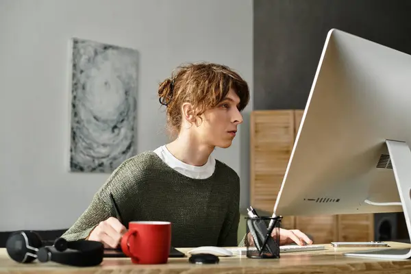 Un jeune étudiant est assis à son bureau, engagé dans l'étude et la gestion des tâches sur son ordinateur à la maison. — Photo de stock