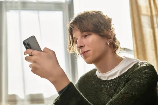 A focused young man relaxes at home, absorbed in his mobile device during leisure time. — Stock Photo