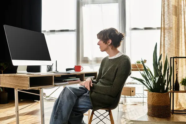 A young man sits thoughtfully at his home workspace, surrounded by plants and natural light. — Stock Photo