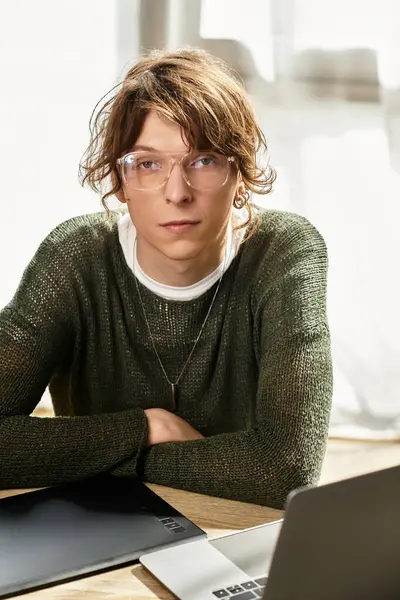 Ein junger Mann sitzt entschlossen an einem Tisch, beschäftigt sich mit dem Lernen, während er von Lernwerkzeugen umgeben ist. — Stockfoto