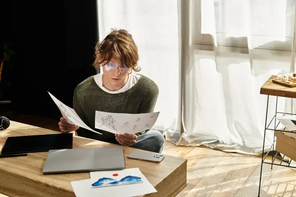 Young man engaged in artistic research, studying various sketches while sitting at home. — Stock Photo