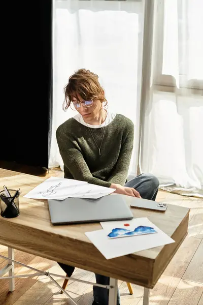 Un jeune homme étudie à son bureau, entouré de croquis et d'un ordinateur portable, profondément concentré. — Photo de stock