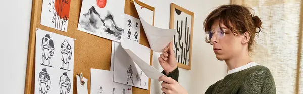 Молодой человек усердно изучает рисунки, отображаемые на пробковой доске, находясь дома. — стоковое фото