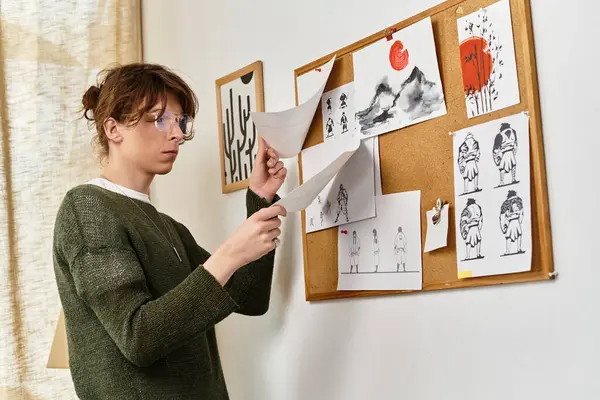 Young man engages in organizing illustrations on a corkboard while focused and at ease in his home. — Stock Photo