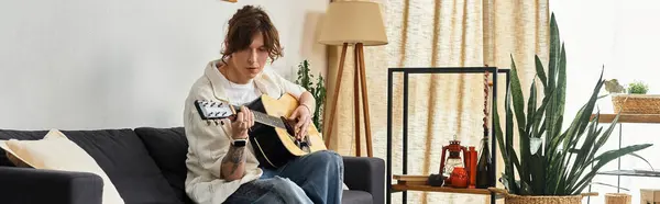 Un giovane uomo si rilassa su un divano a casa, suonando la chitarra e godendo la musica. — Foto stock
