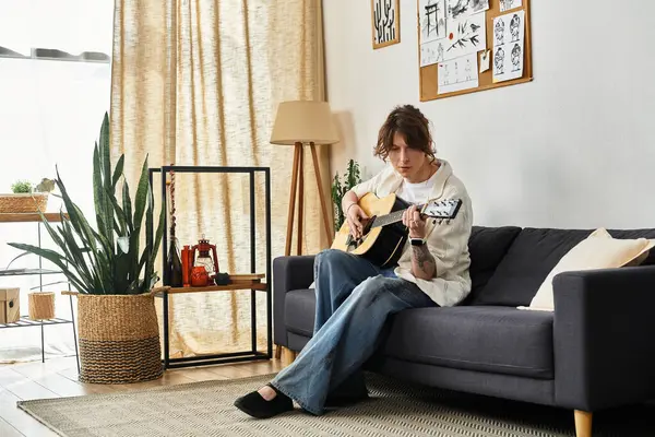 Un giovane si siede comodamente su un divano, suonando la chitarra mentre è circondato da decorazioni e piante. — Foto stock