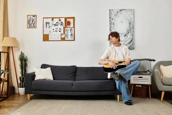 Um jovem relaxa em um sofá, praticando guitarra em uma casa elegante com decorações artísticas. — Fotografia de Stock