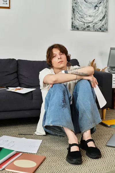 A young man sits comfortably at home, lost in thought amidst scattered study materials on the floor. — Stock Photo