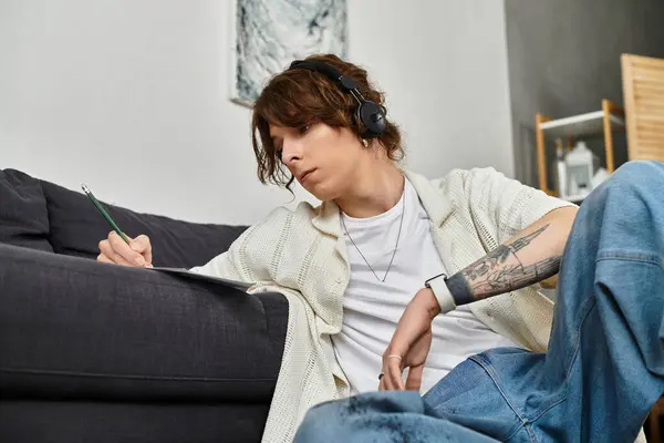 A young man sits on a couch, studying with pencil and paper at home. — Stock Photo