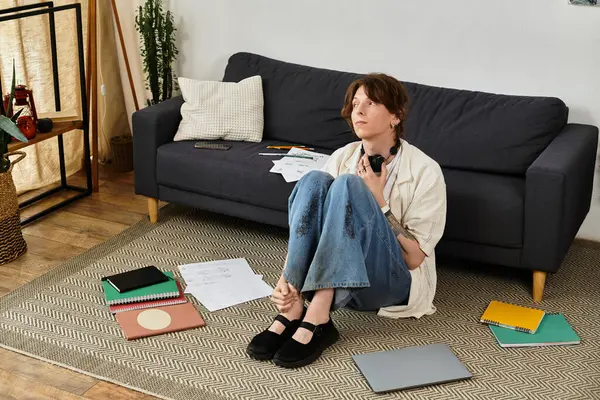 A young man sits on the floor, pensively surrounded by scattered papers and gadgets. — Stock Photo
