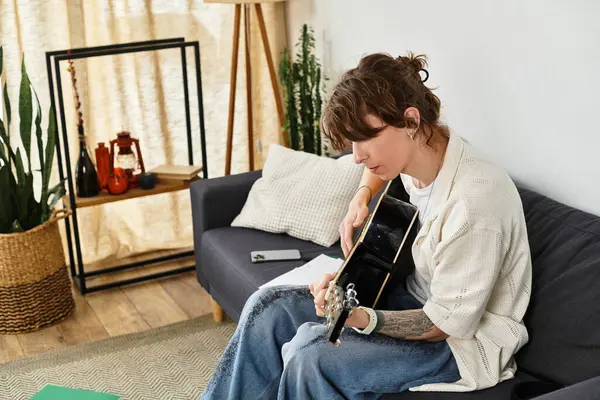 Un joven se sienta cómodamente en su sala de estar, rasguñando su guitarra y enfocado en su música. - foto de stock