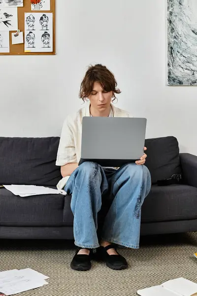 Konzentrierter junger Mann sitzt tagsüber mit Laptop auf der Couch, während er zu Hause studiert — Stockfoto