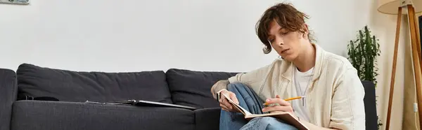 Focused young man sits in his living room, actively writing notes in a notebook on a casual day. — Stock Photo