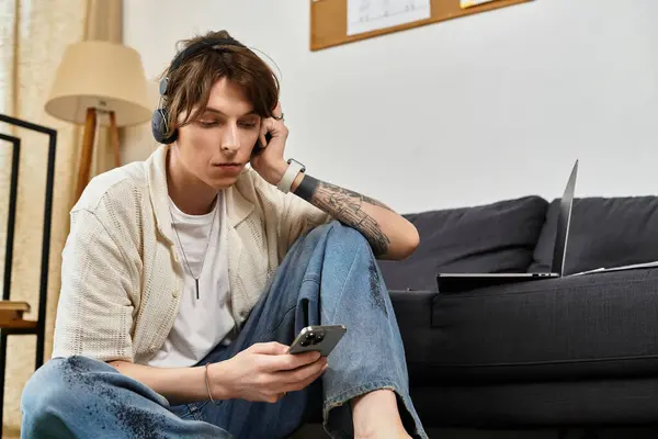 A young student relaxes at home, focused on his phone while listening to music through headphones. — Stock Photo