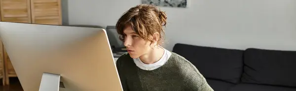 Joven estudiante masculino intensamente comprometido en sus estudios desde la comodidad de su espacio de trabajo en casa - foto de stock