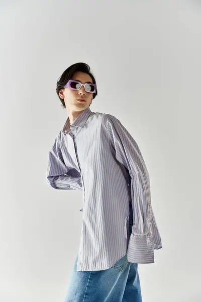 A young non binary person showcases trendy style with confidence against a neutral backdrop. — Stock Photo