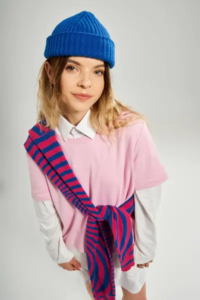 In a vibrant studio, a young woman showcases her unique style with a blue beanie and playful outfit. — Stock Photo