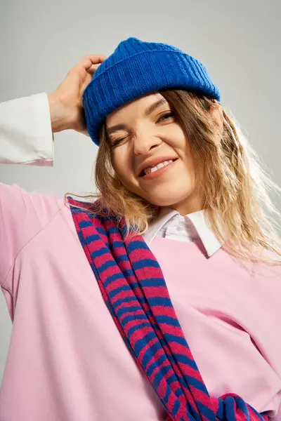 Eine junge Frau lächelt selbstbewusst, während sie ihr trendiges Outfit und ihren blauen Beanie-Hut präsentiert. — Stockfoto