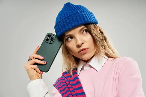 A young woman showcases her fashionable style in a studio, thoughtfully posing with a smartphone. — Stock Photo