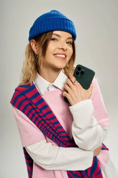 In a bright studio, a young woman smiles and showcases her style with a smartphone. — Stock Photo