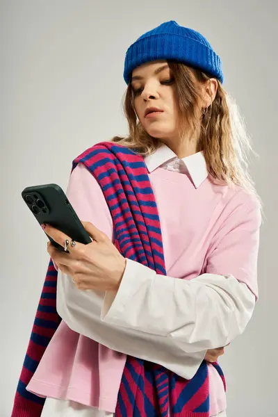 A stylish young woman in a blue beanie and colorful outfit checks her phone in a studio. — Stock Photo