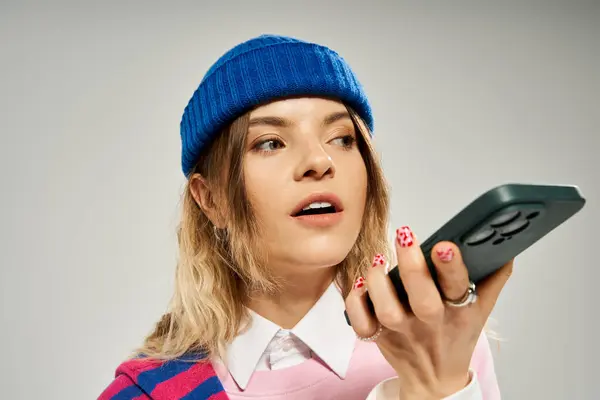 Pretty woman in a blue beanie engages with her smartphone, exuding youthful charm and style. — Stock Photo