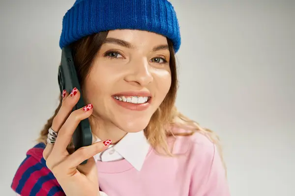 Pretty young woman wearing a blue beanie hat chats happily on her phone, radiating confidence. — Stock Photo