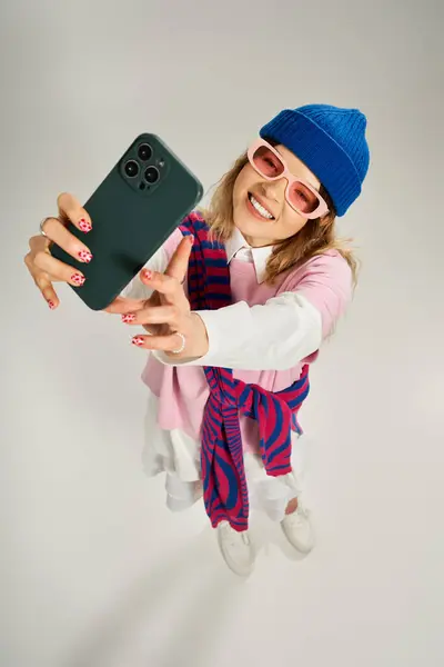 A youthful woman in a vibrant outfit poses playfully with a smartphone, showcasing her style. — Stock Photo